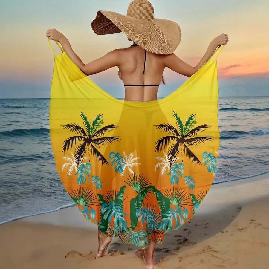 Woman on a beach holding a yellow tropical patterned sarong with a sunset in the background