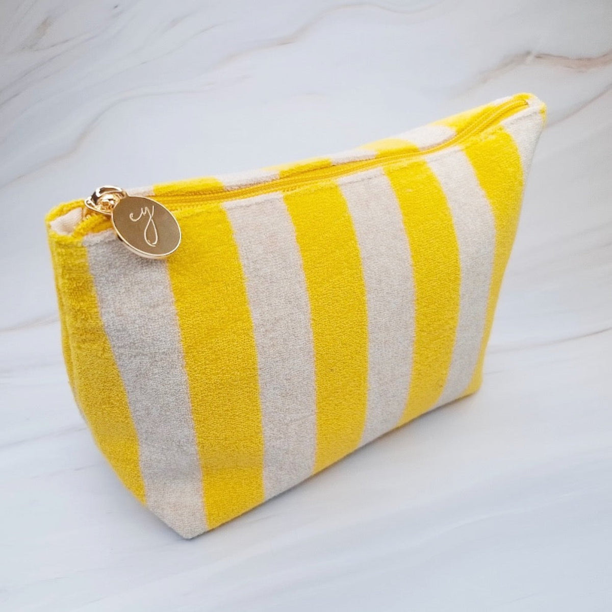 Yellow and white striped pouch with a gold tag on a light background
