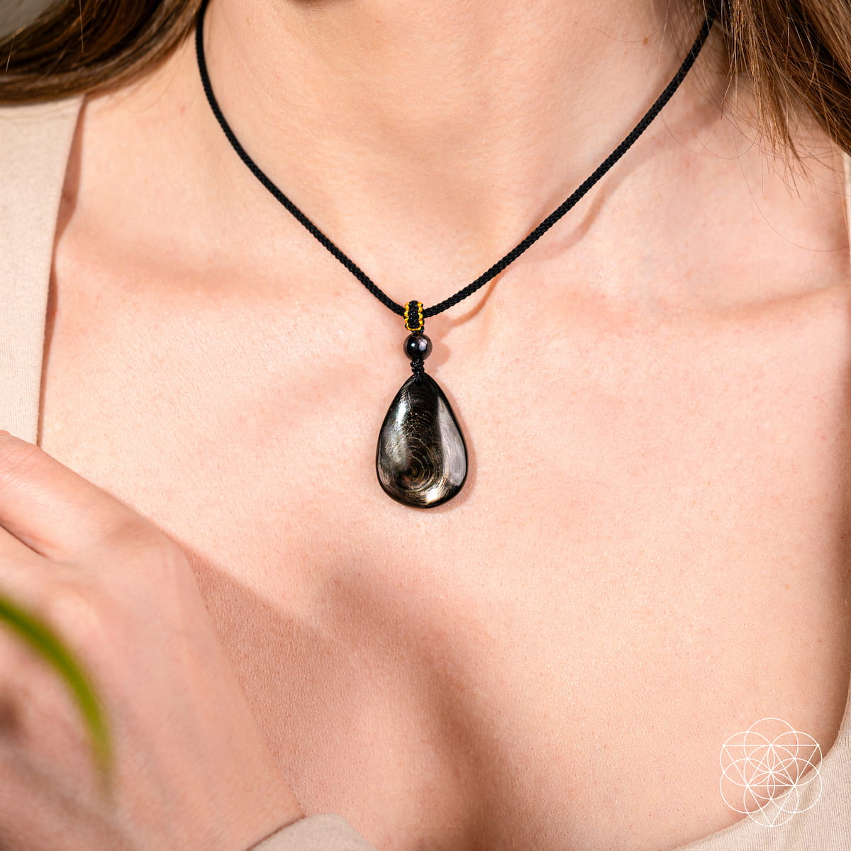 Teardrop-shaped pendant on a black cord necklace worn by a person. The ﻿Hypersthene Millionaire Manifestation Pendant. Rare Egyptian Wealth Stone.