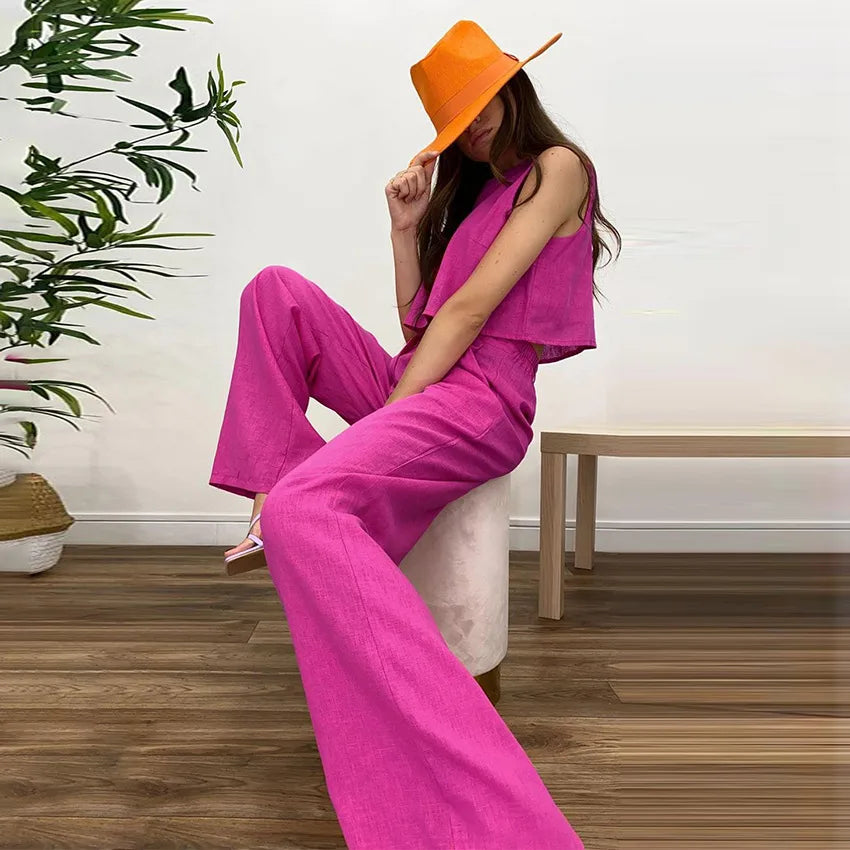 Woman in a bright pink outfit and orange hat sitting on a chair indoors.