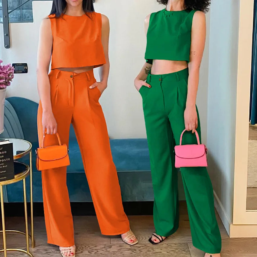 Two women in orange and green outfits with matching handbags indoors.