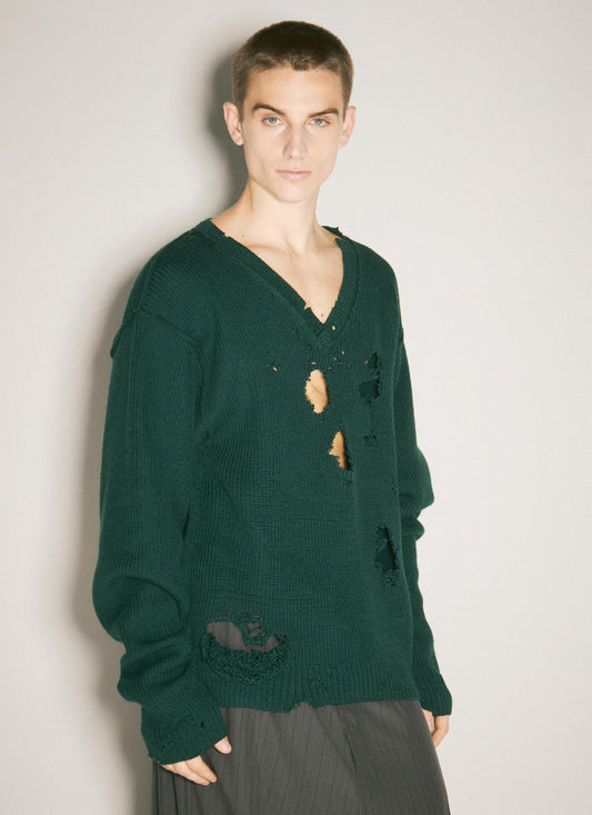 A person modeling a dark green Vetements distressed wool V-neck sweater with long sleeves and ribbed trims, captured against a clean, neutral background.