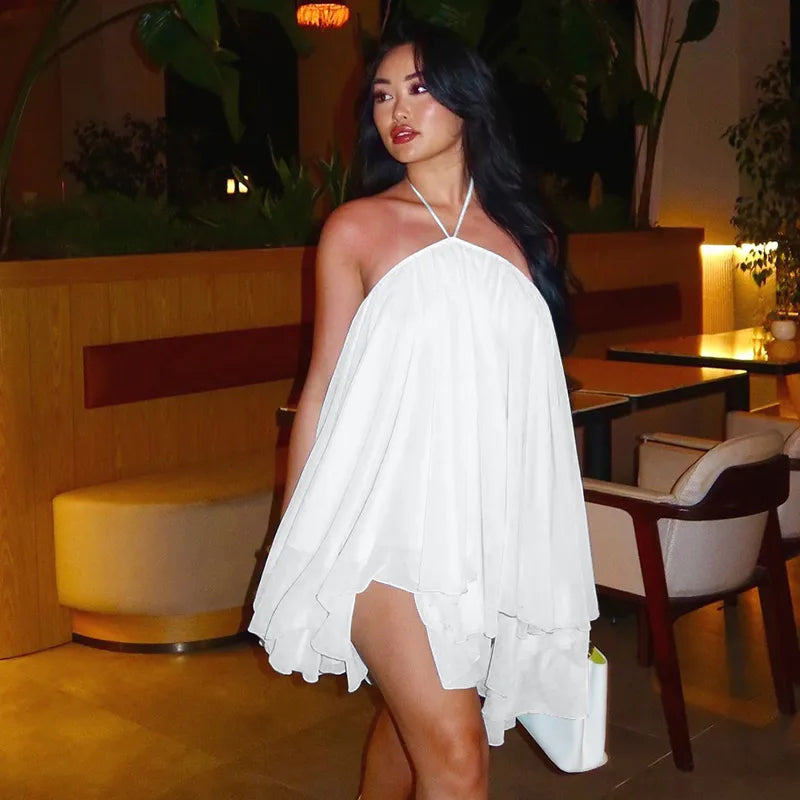 Woman in a white dress standing in an indoor setting with plants and furniture.