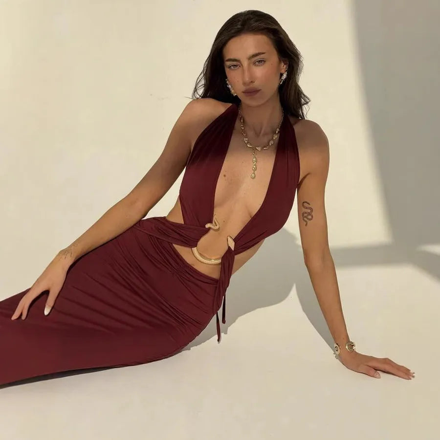 Woman in a burgundy dress with gold jewelry against a neutral background
