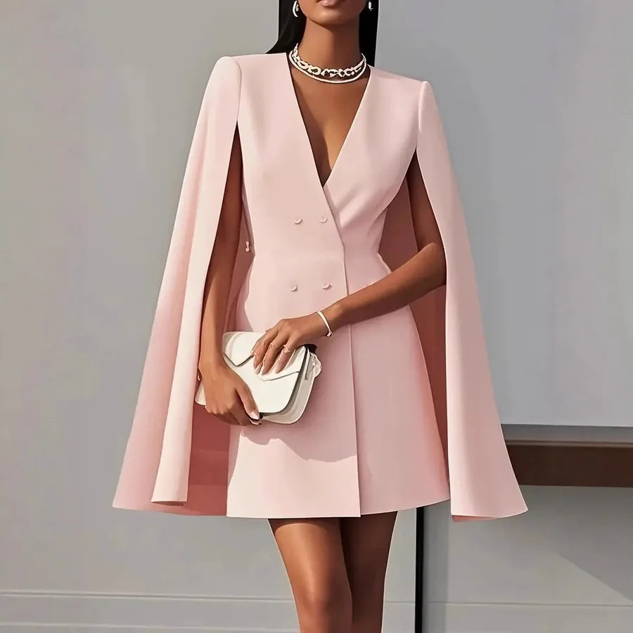 Woman wearing a pink cape dress holding a white clutch against a gray background. Light Pink Blush Pink Blazer Coat Dress