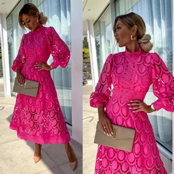 Woman wearing a pink lace dress holding a beige clutch in front of a modern building.