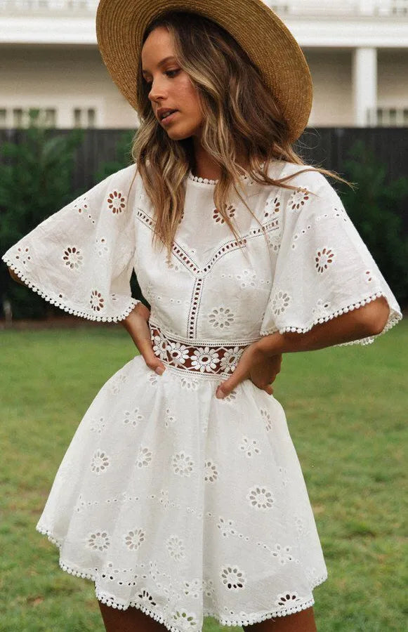 Woman wearing a white dress with floral patterns and a straw hat outdoors.