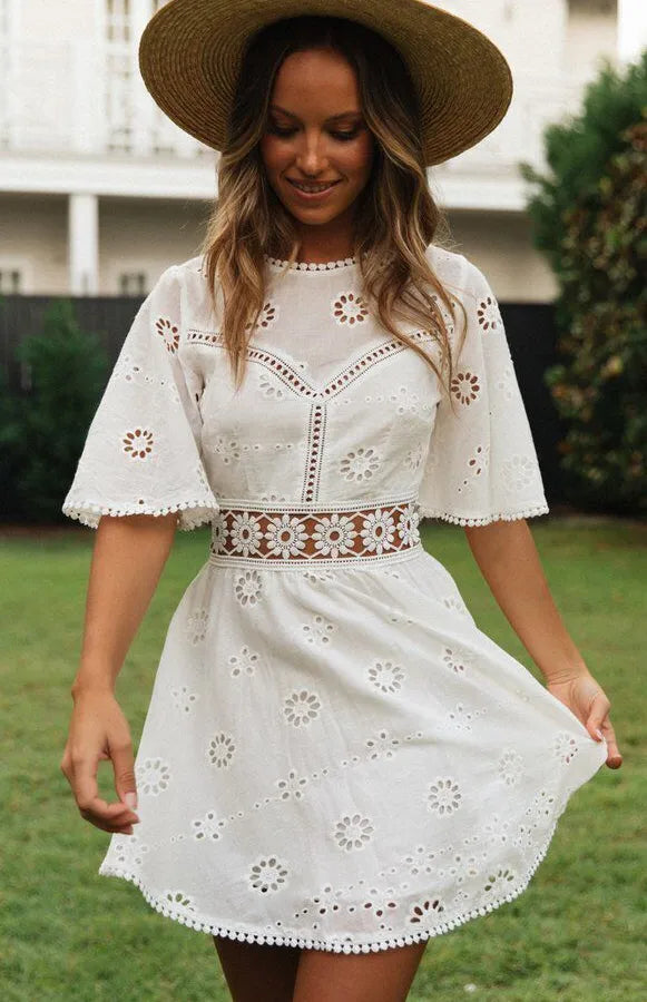 Woman wearing a white embroidered dress with a brown hat outdoors.
