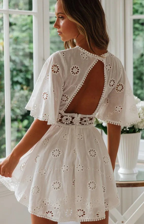 Woman wearing a white lace dress with a floral pattern in a bright room.