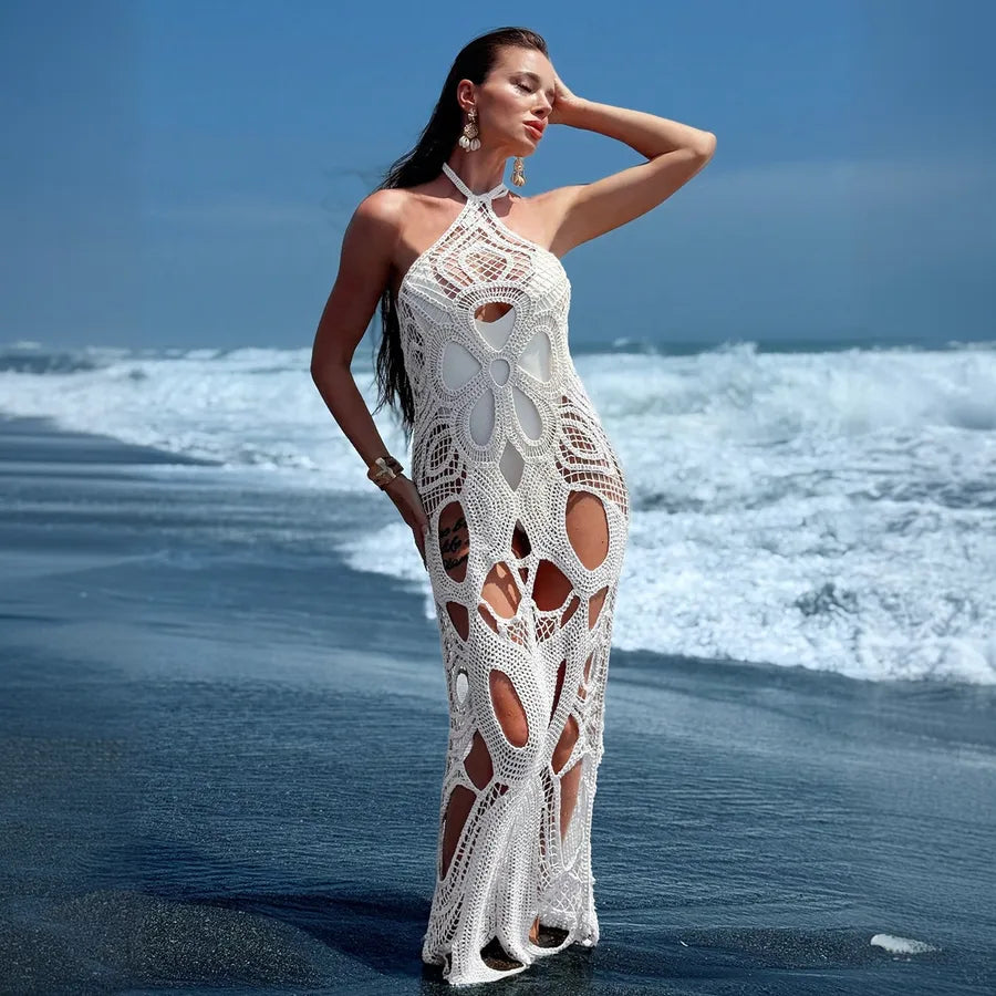 Woman in a white crochet dress standing on a beach with waves in the background