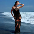 Woman in a black crochet dress standing on a beach with waves in the background