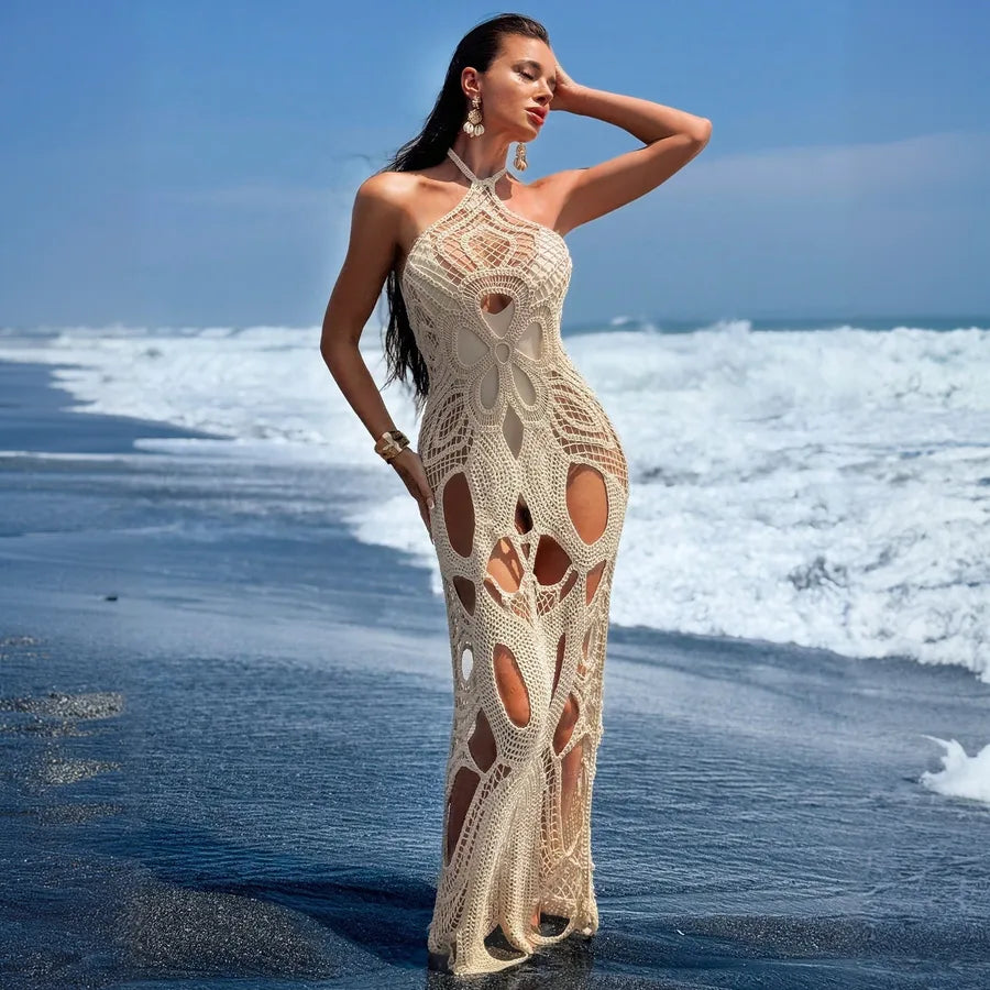Woman in a crochet dress standing on a beach with waves in the background