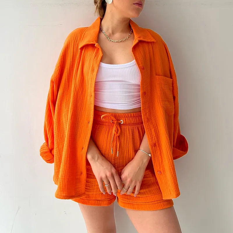 Person wearing an orange outfit long sleeve orange shirt on a cream colored background. orange drawstring shorts set.