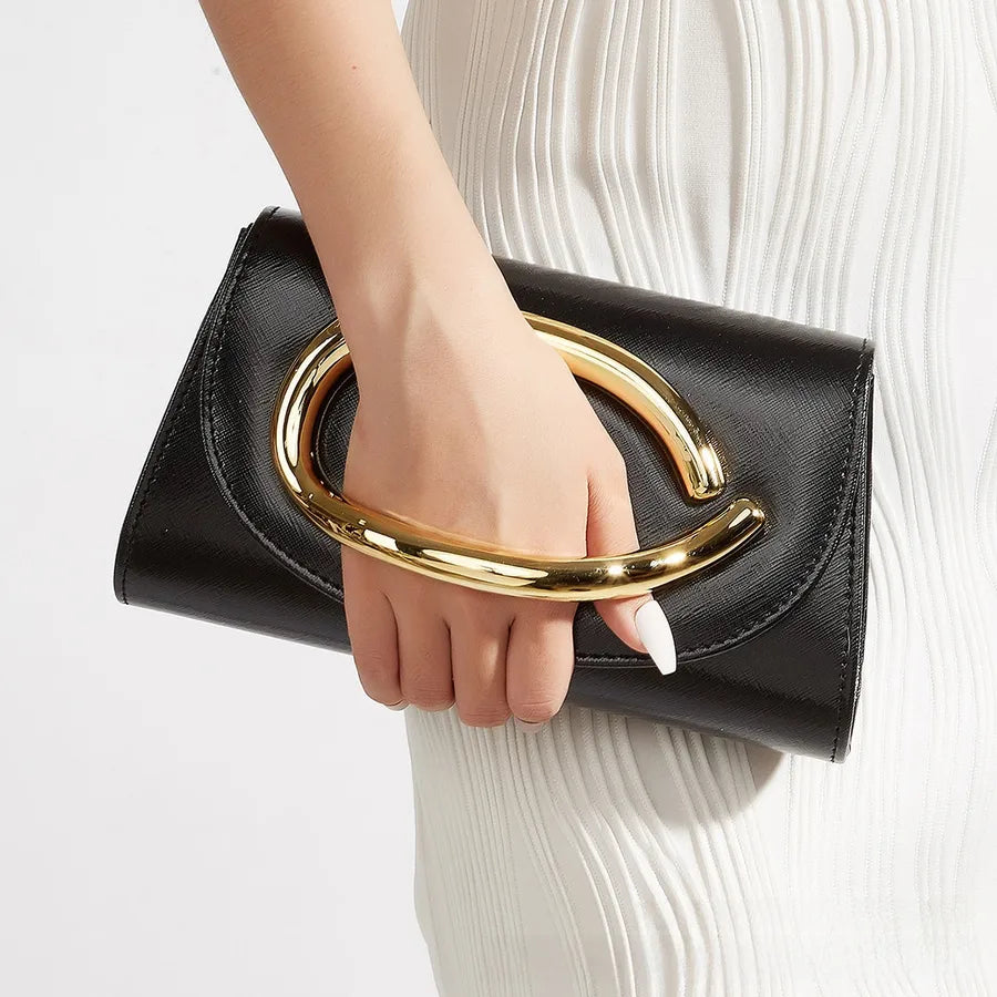 Black clutch with gold handle held by a hand on a light gray background