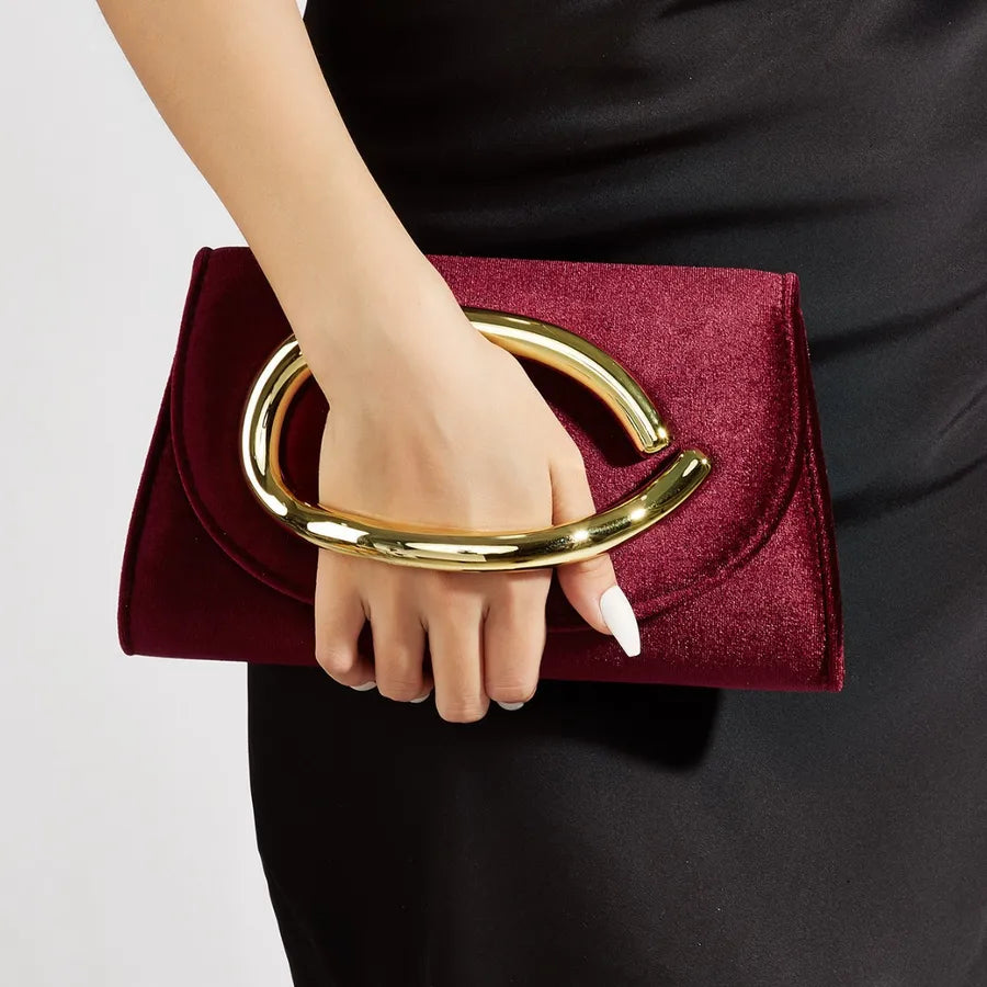 Hand holding a burgundy clutch with a gold handle against a neutral background