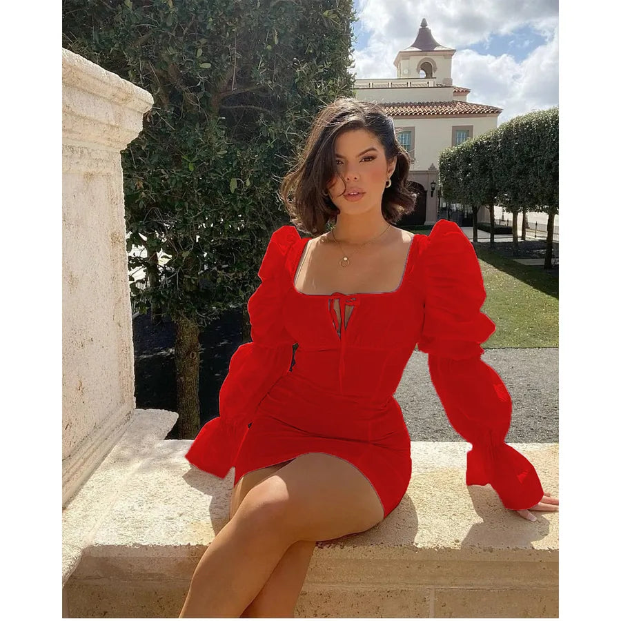 Woman in a red dress sitting outdoors with a building and trees in the background
