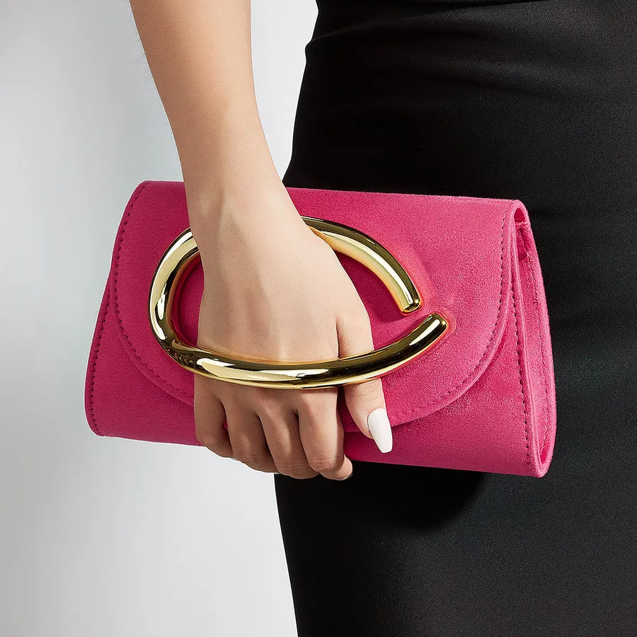 Hand holding a pink clutch with gold handle against a neutral background