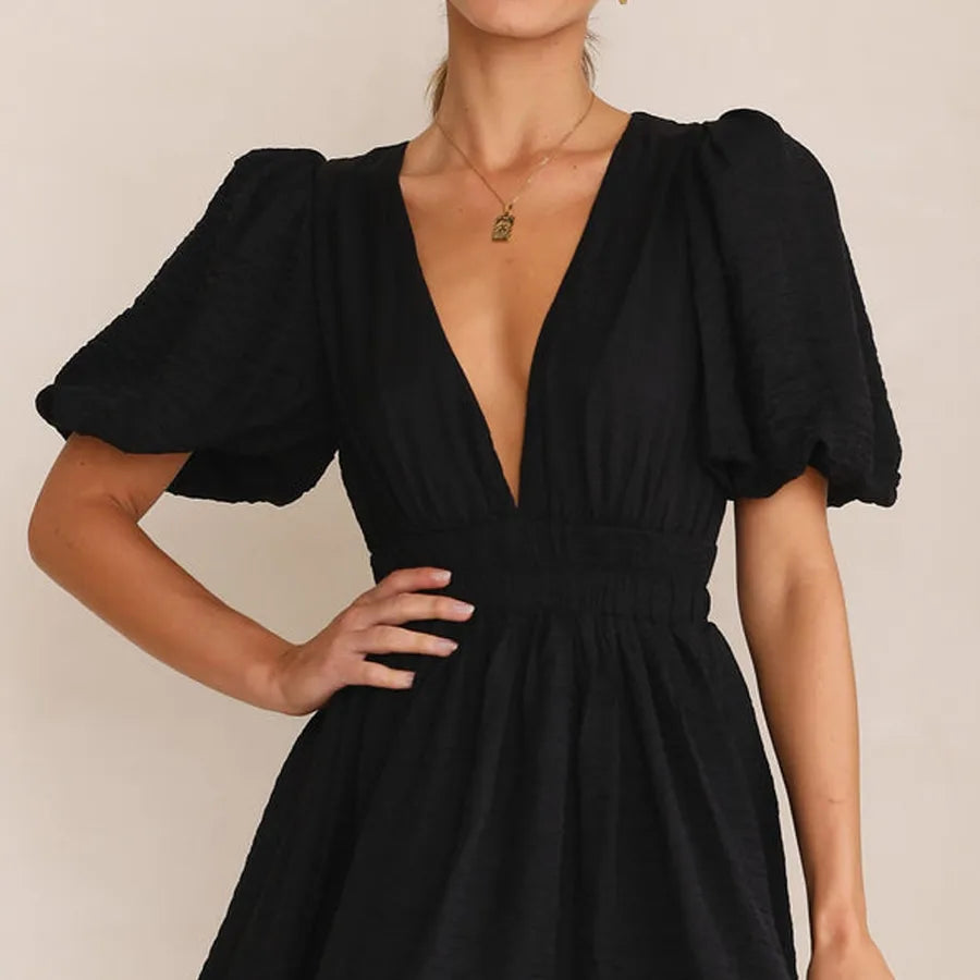 Black dress with puff sleeves worn by a model on a plain background