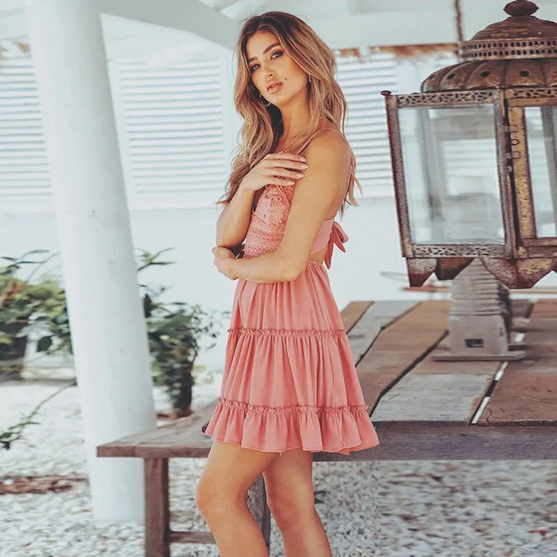 Woman in a pink dress standing in a sunlit outdoor setting with plants and a wooden table.
