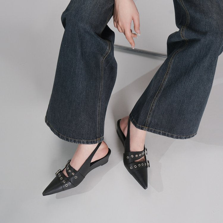 Black pointed-toe slingback flats with silver-tone eyelet and buckle details, shown on a model wearing dark blue wide-leg jeans against a light gray studio background.