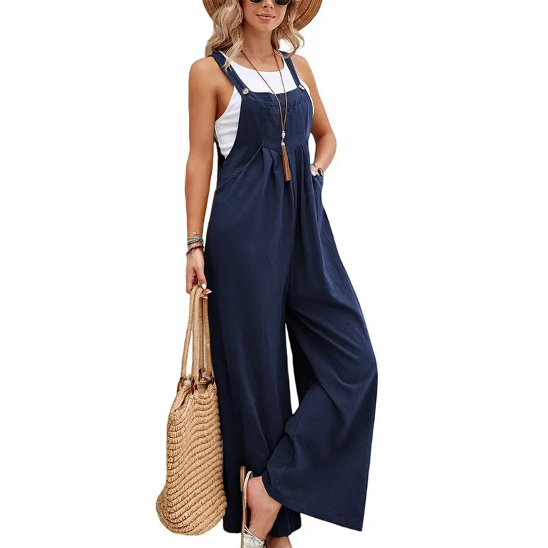 Woman wearing a navy blue jumpsuit with a white top, holding a straw bag on a white background.