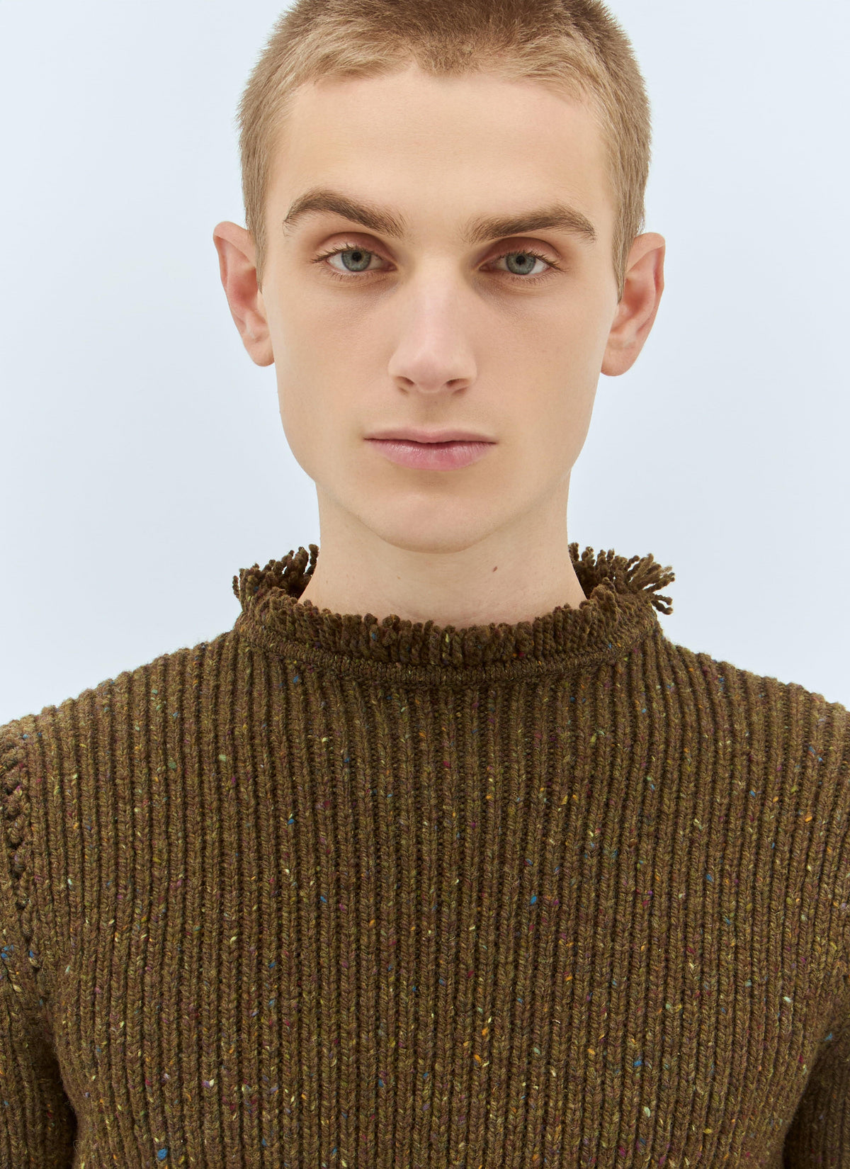 Person wearing a brown ribbed sweater against a light blue background