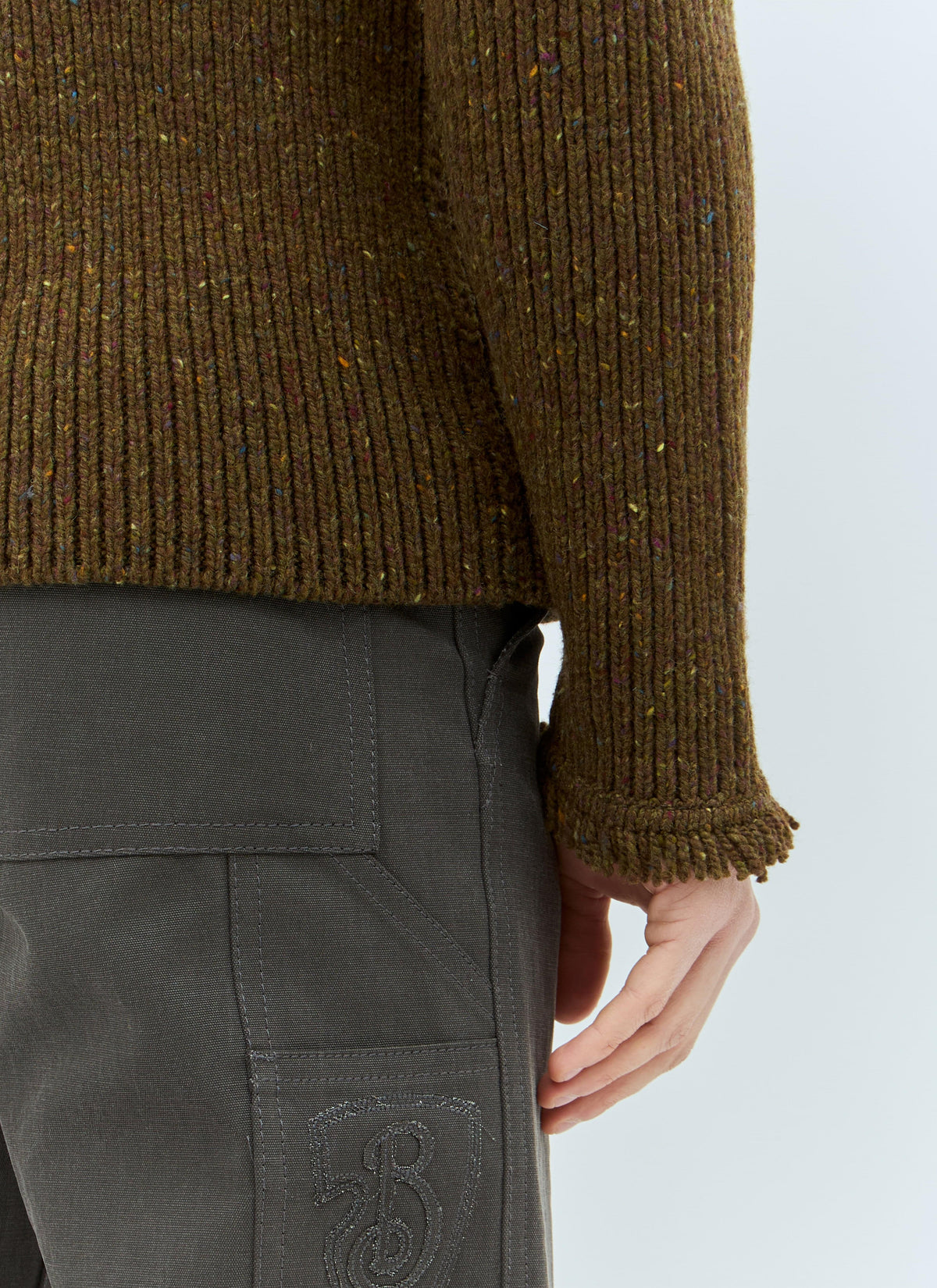 Brown ribbed sweater and dark pants with a brand logo on a light gray background