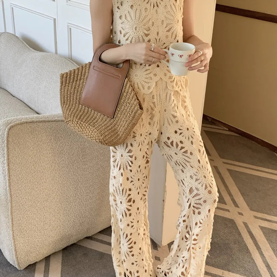 Person wearing a beige crochet outfit holding a cup and a woven bag in a room.