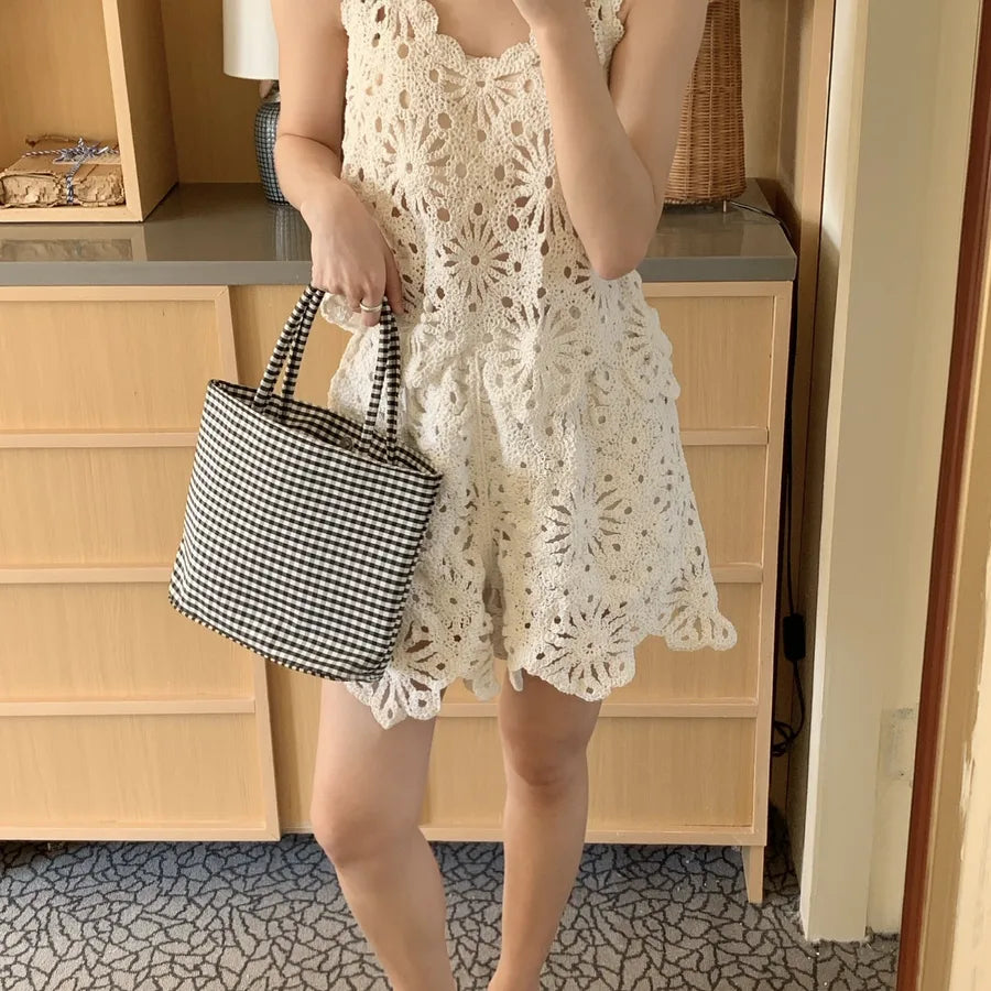 Person wearing a white lace dress holding a black and white checkered bag indoors.