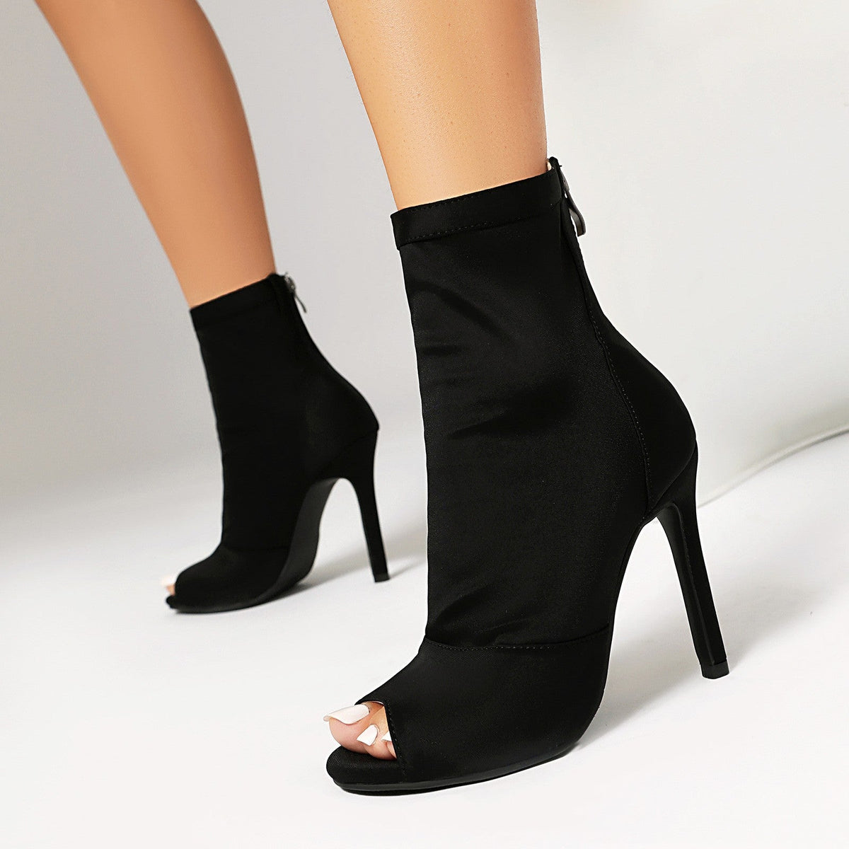 Black high-heeled open-toe ankle boots on a neutral background