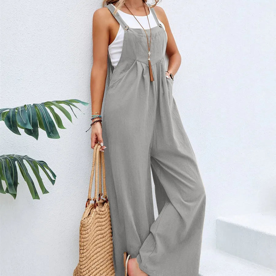 Woman wearing a gray jumpsuit with a white top, holding a straw bag against a light background.