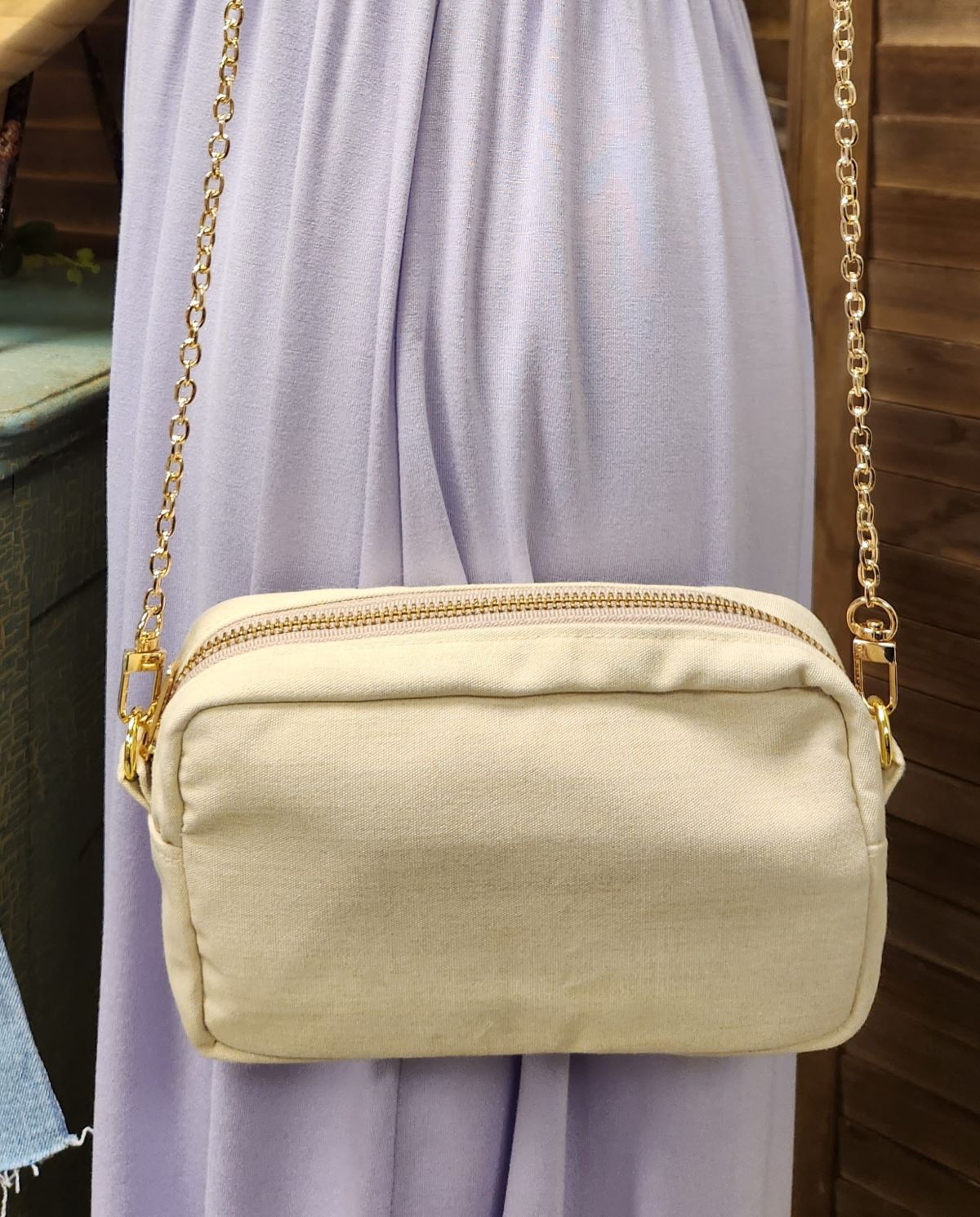 Beige handbag with gold chain strap against a light purple curtain background