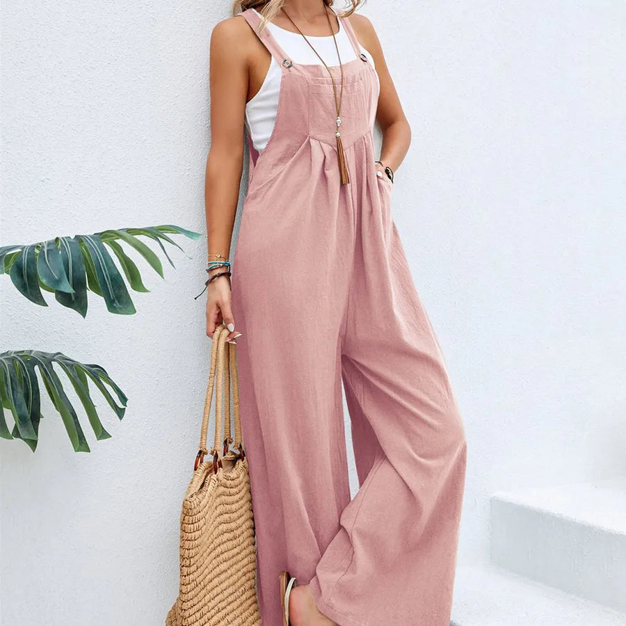 Woman wearing a pink jumpsuit with a white top, holding a straw bag against a light background.