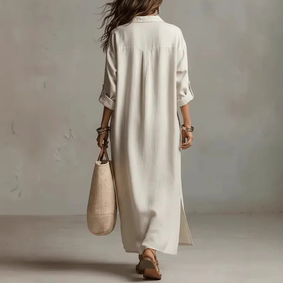 Person wearing a long beige dress holding a woven bag against a plain background