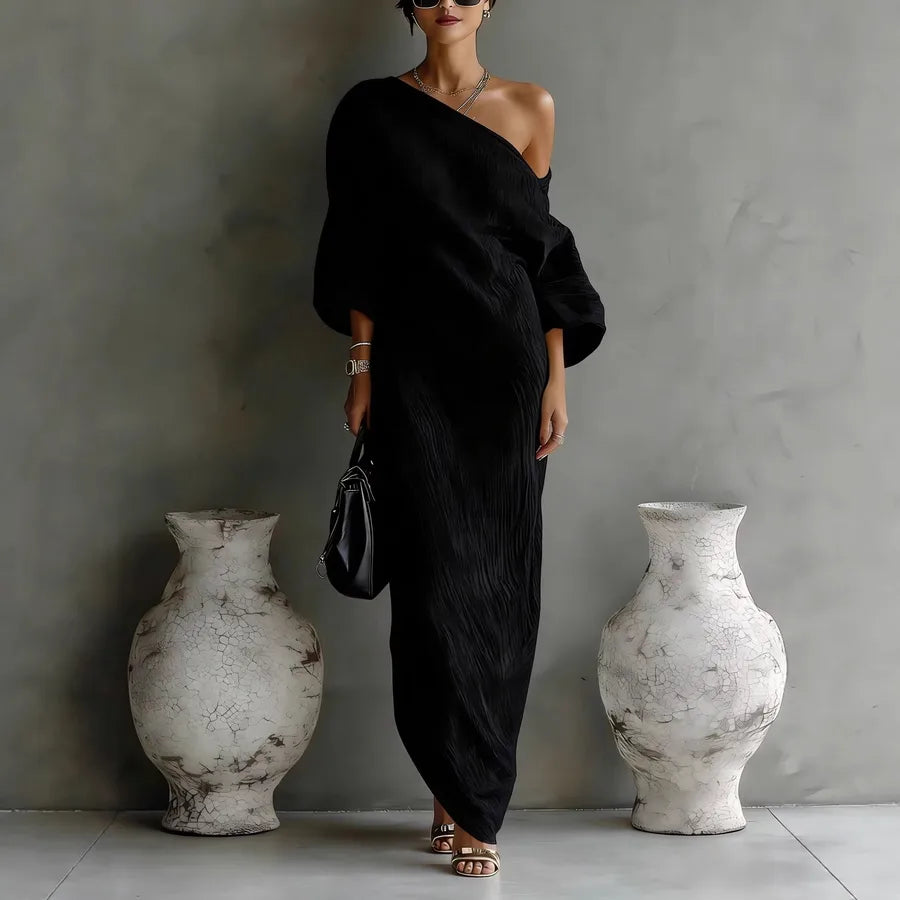 Woman in a black off-shoulder dress standing between two large white vases against a gray wall.