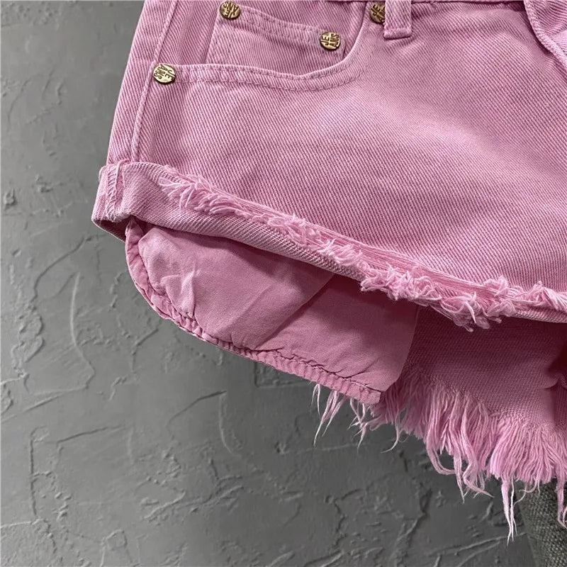 Close-up of pink denim shorts with frayed edges on a gray textured background