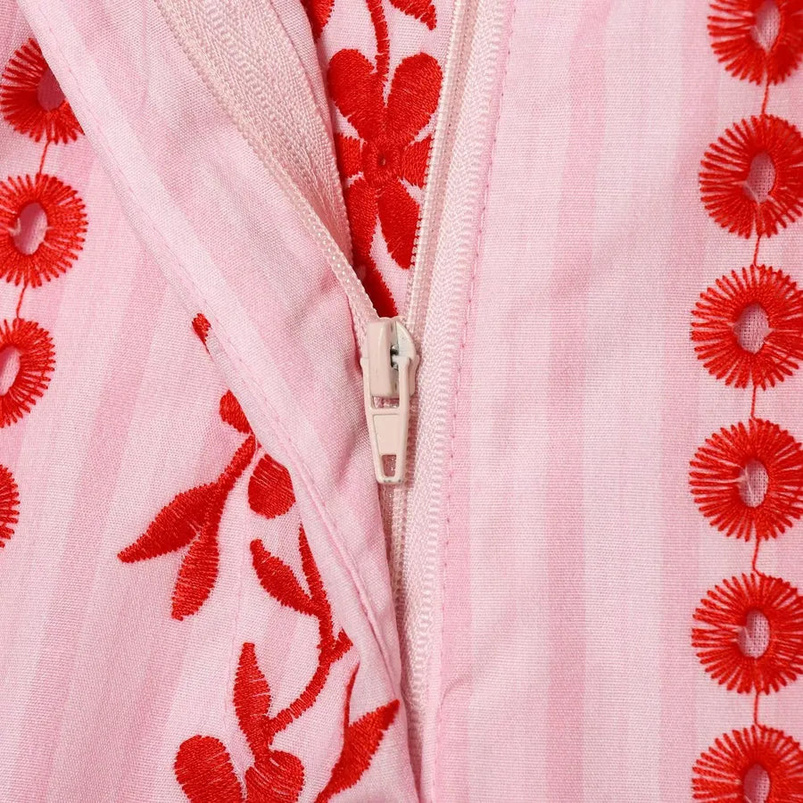Close-up of a pink fabric with red floral embroidery and a zipper. pink pants with red flowers