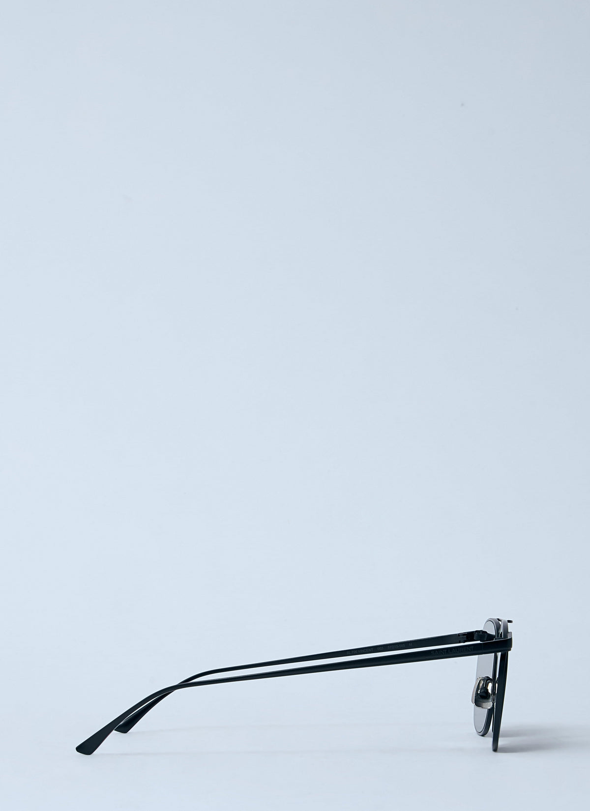 Black metal-framed sunglasses with a single round lens, shown lying on their side against a light gray background.
